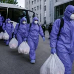 People in hazmat suits disembarking bus
